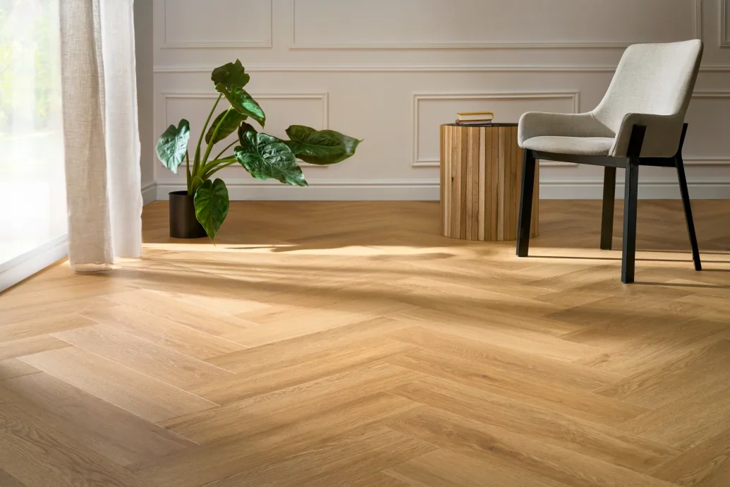 Arbiton Menor Eiche als Fischgrät-Vinylboden neben einem hellen Sessel im Wohnraum. Entdecken Sie Arbiton-Designböden und besprechen Sie Ihre gewünschte Raumwirkung mit uns. Arbiton Menor Eiche als Fischgrät-Vinylboden neben einem hellen Sessel im Wohnraum